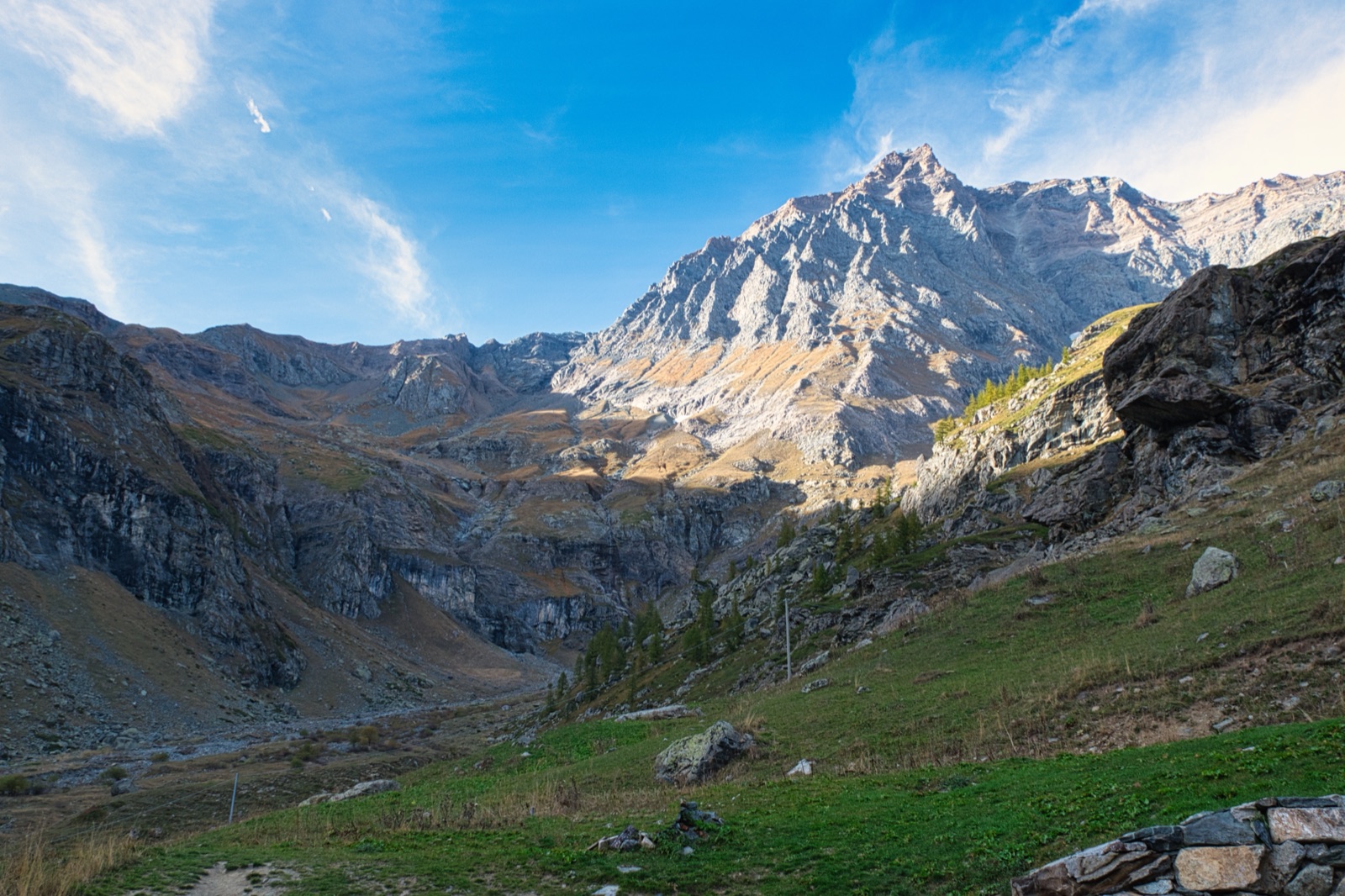 Cima rocciosa illuminata dal sole in fondo a una valle verde, tra pareti di montagna