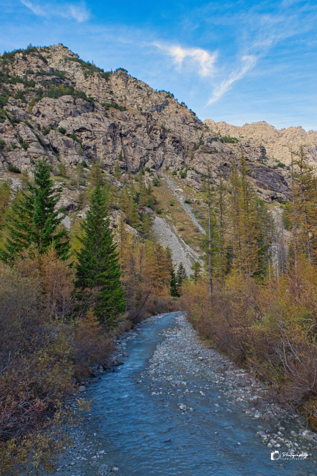 Torrente dalle acque chiare tra larici autunnali, ai piedi di pareti rocciose