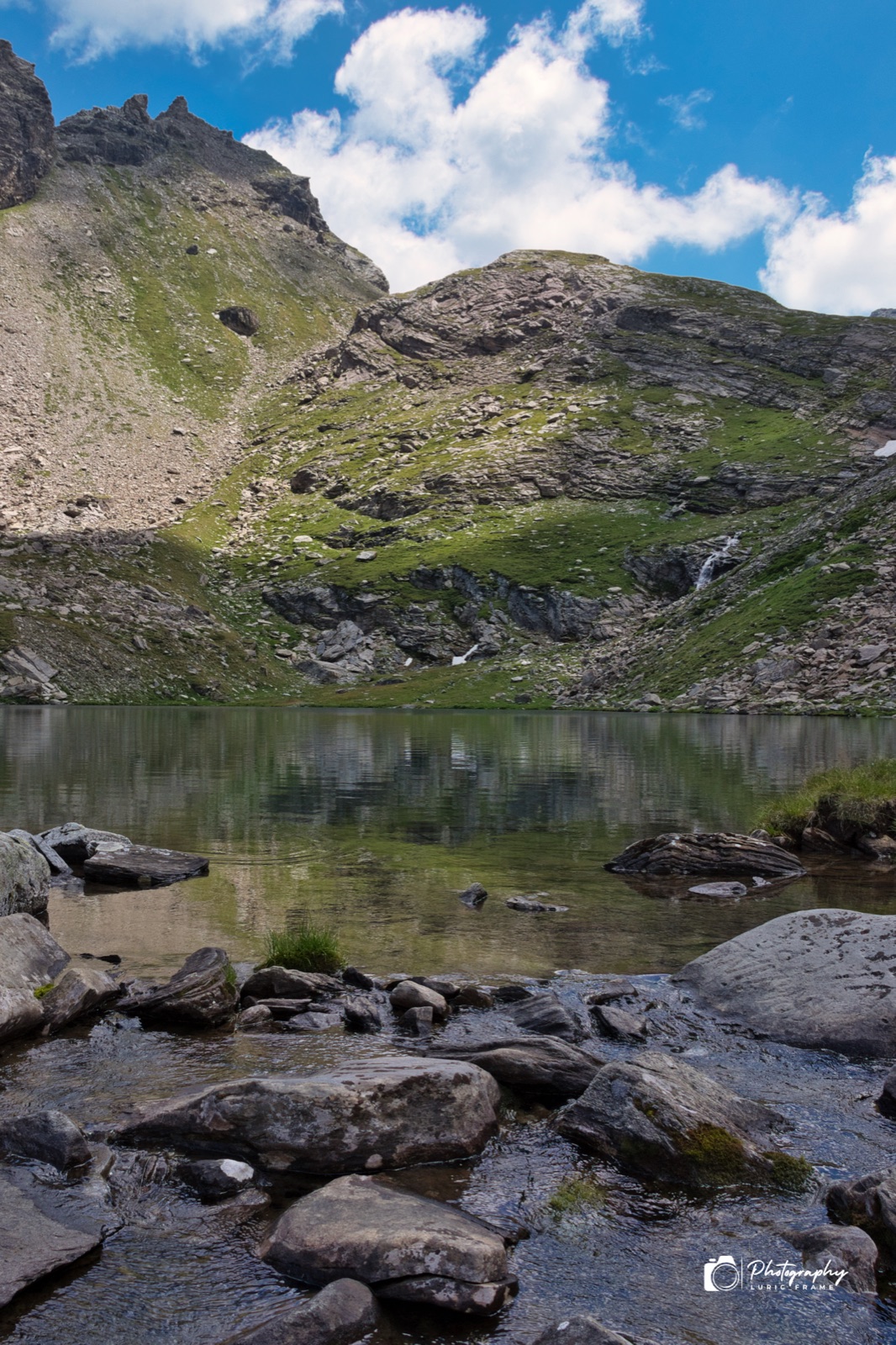 Lago alpino con massi in primo piano e montagne rocciose che si specchiano nell'acqua
