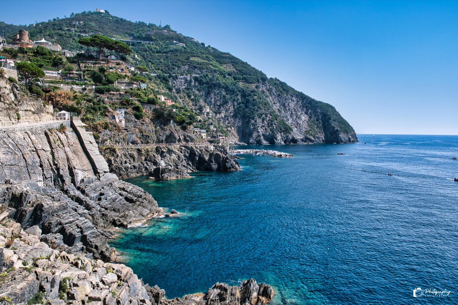 Costa rocciosa e mare blu intenso sotto una collina verde, in una giornata limpida