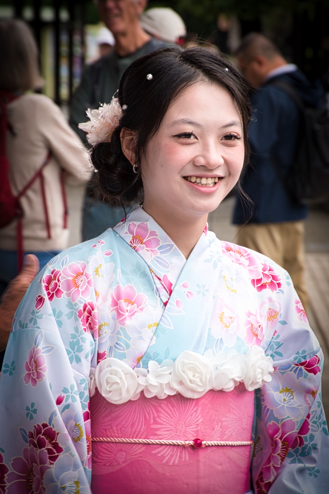 Ragazza sorridente in kimono azzurro chiaro a fiori rosa, con un fiore bianco tra i capelli raccolti