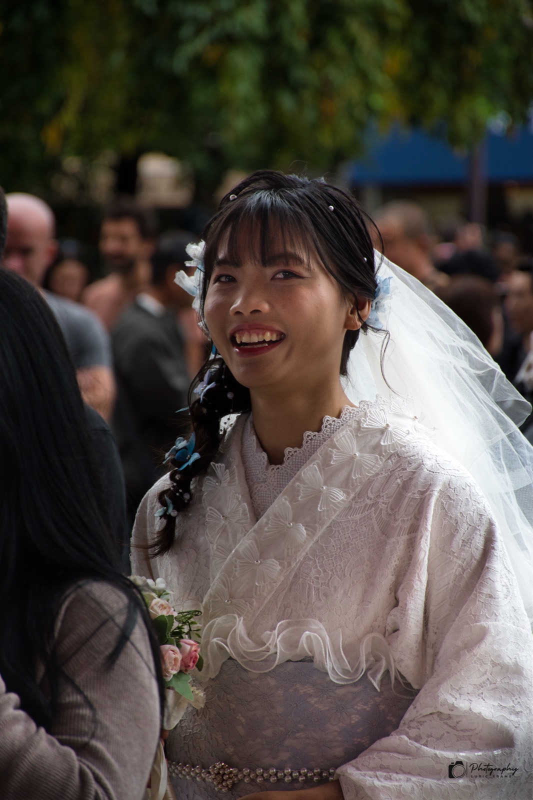 Donna sorridente in kimono chiaro con un velo bianco, tra la folla