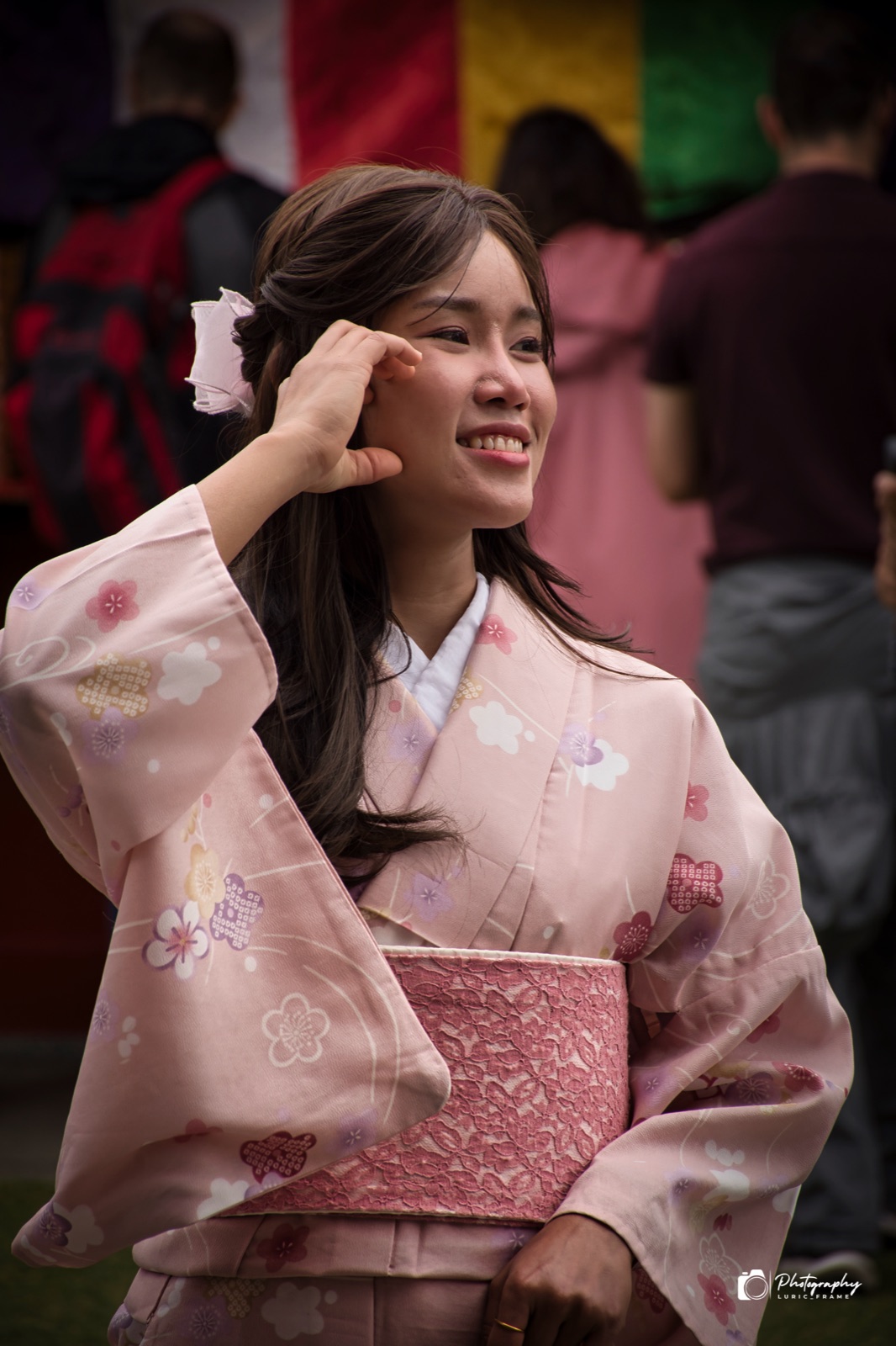 Ragazza sorridente in kimono rosa che si sistema i capelli, con un fiore bianco all'orecchio